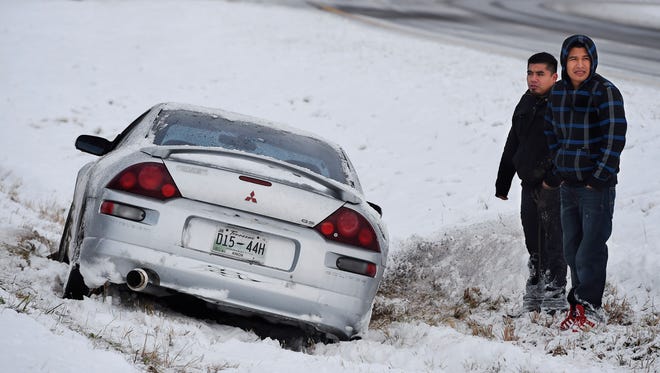 Stranded on the median, Angel Abendano, left, and Santiago Cuevas wait for assistance after losing control of their vehicle on the Pennyrile Parkway Monday, Nov. 17, 2014 after the first snow storm of the season dropped upwards of 5 inches of snow and ice on the area, closing schools.