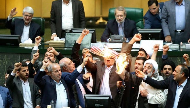 A handout picture made available by the Iranian parliament office shows Iranian lawmakers burn a U.S. flag during the parliament session in Tehran.