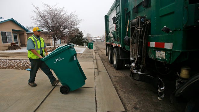 Armando Ortiz, a driver with Waste Management, carries a trash can to his truck on Wednesday on Wellington Street in Farmington.