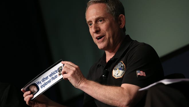 Alan Stern, principal investigator of NASA's New Horizons mission team, holds up a bumper sticker while delivering remarks during a press briefing. Stern testified in front of Congress on July 28, 2015, about the New Horizons mission.