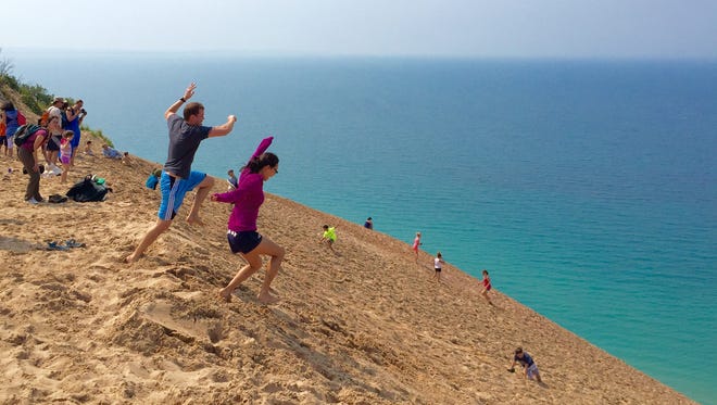 A couple takes a leap of faith at Michigan's iconic Sleeping Bear Dunes in Empire. Visitors walk part of the giant dune along Pierce Stocking Drive. Lake Michigan meets the dune at the shoreline in late August 2015. 