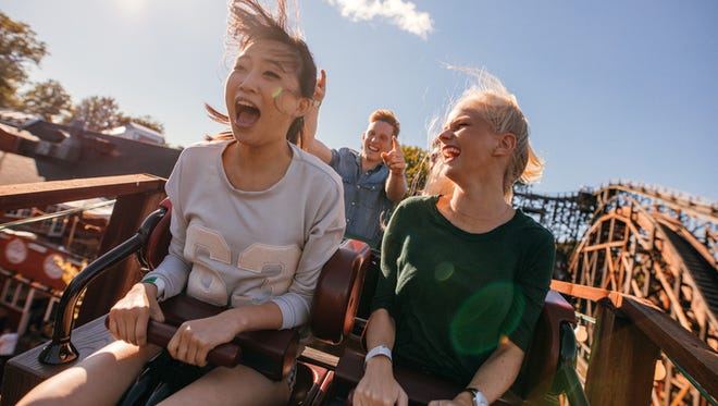 Young friends on thrilling roller coaster ride. Young women and men having fun at amusement park.