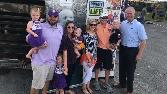 The Perrys and Boswells appear at a Donate Life event with Jay Jacobs, Auburn athletic director, before the LSU and Auburn game on Saturday, October 14. The face of John Clarke Perry appears on a poster in the background.