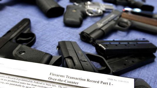 A federal firearms transaction record, which includes a background check, lays near a selection of guns at Ron's Pawn and Gun in Des Moines in 2013.