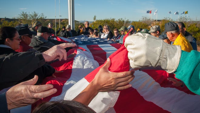 Veterans and visitors to Veterans Memorial Park on Veterans Day unfurl Las Cruces’ garrison flag prior to it being raised.