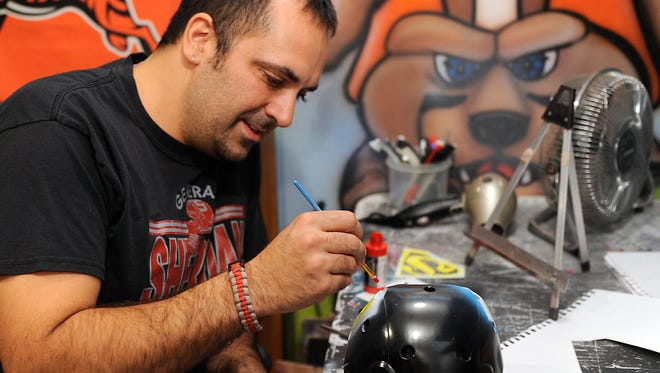 Stephen Gioffre paints Superman's emblem on a helmet for a child in his home studio. Gioffre, an art teacher at Sheridan High School, recently started using his painting and airbrushing skills to help families dealing with medical issues.