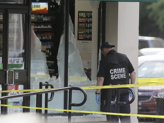 A crime scene investigator looks a shot out windows