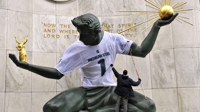 Amid wind and rain Monday Ryan Wheeler of Prop Art Studio in Detroit ensures a good fit of the Michigan State Spartans jersey on the statue outside Detroit’s City Hall.