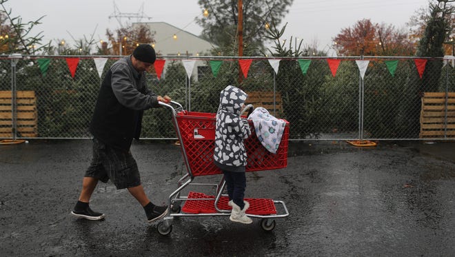 Journey Harlan, 4, catches a ride with her sister, Maysson Harlan, 9 months, as her father, Dana Harlan, pushes their shopping cart on a wet Friday after buying a Christmas tree at Johnson's Family Christmas Trees in Redding.