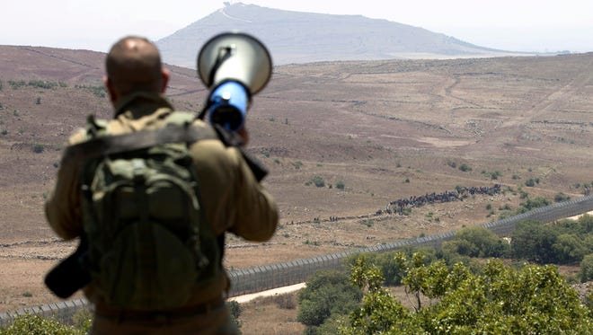 Israeli soldier uses a speaker to communicate with Syrian Refugees marching towards the Israeli Security fence demanding help on the Syrian side of the Golan Heights in Quneitra province, as seen from the Israeli side of the border. 