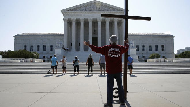 Tom Alexander holds a cross as he prays prior to rulings outside the Supreme Court on Capitol Hill in Washington, Wednesday, July 8, 2020.  The Supreme Court is siding with two Catholic schools in a ruling that underscores that certain employees of religious schools, hospitals and social service centers can't sue for employment discrimination.
