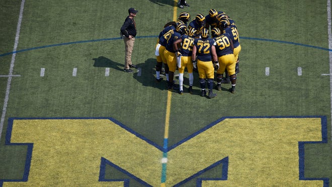 Michigan football huddles with coach Jim Harbaugh watching during the team's 2017 spring game.