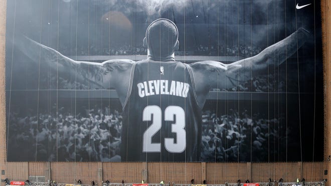 FILE - In this Oct. 30, 2014, file photo, workers finish hanging a mural of Cleveland Cavaliers' LeBron James on a building in Cleveland. The colossal LeBron James banner is getting a small _ but significant _ upgrade.
The iconic, 10-stories-tall mural is being removed this week and replaced with a new one that includes a gold patch of the Larry O’Brien Trophy on the back of James’ uniform to represent the Cavaliers winning the NBA title last season to end the city’s 52-year championship drought.
The new banner is expected to be installed by Friday, Oct. 21, 2016. (AP Photo/Mark Duncan, File)
