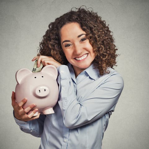 Smiling woman putting money into piggy bank.
