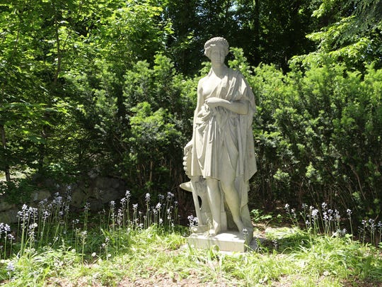 An impressive Westerly granite statue of “Industry” at the end of an allee of bluebells and hostas. She is clothed in classical robes, with the attributes of ancient industry at her feet: anvil, hammer and the cogwheel symbolizing 19th-century mechanized production, American, ca. 1880.