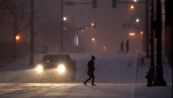 Pedestrians walk across a snowy street in downtown Kansas City, Mo., on Saturday, Dec. 17, 2016. A winter storm of snow, freezing rain and bone-chilling temperatures hit the nation's midsection and East Coast on Saturday.