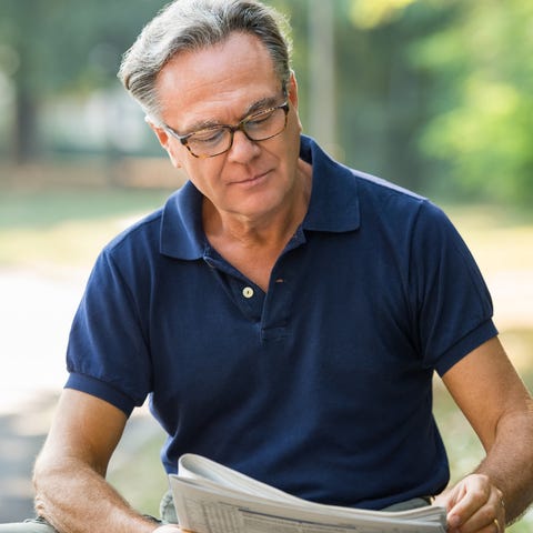 Older man reading newspaper outdoors