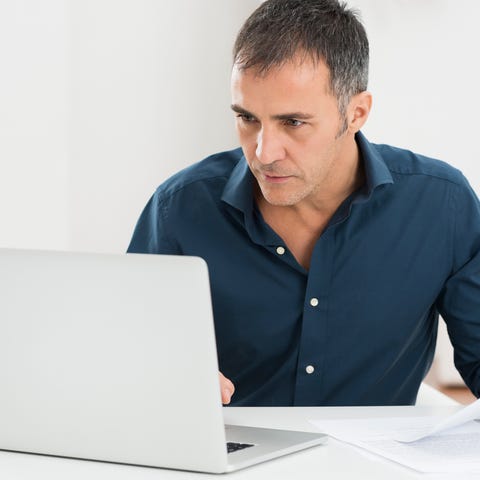 A man sits looking at a laptop monitor, while...