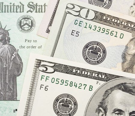 Tax refund check with bills of U.S. currency on top.