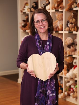 Executive director of Memphis Child Advocacy Center, Virginia Stallworth, holding one of the 12-inch wooden hearts used in Works of Heart. Behind her is the "bear wall" where all children who come through the center get to pick out a bear of their own.