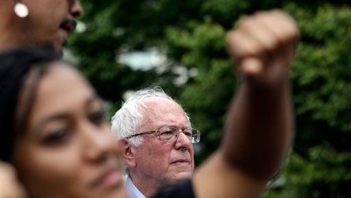 Mara Jacqueline Willaford, left, holds her fist overhead as Democratic presidential candidate Sen. Bernie Sanders, I-Vt., stands nearby at a rally Saturday, Aug. 8, 2015, in downtown Seattle. Willaford and another co-founder of the Seattle chapter of Black Lives Matter took over the microphone just after Sanders began to speak and refused to relinquish it. Sanders eventually left the stage without speaking further and instead waded into the crowd to greet supporters. (AP Photo/Elaine Thompson)