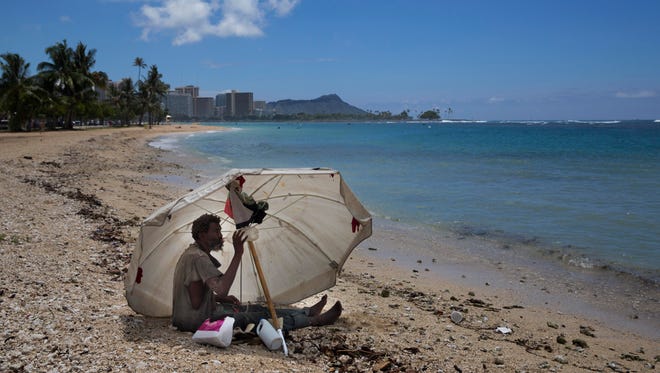 In this 2015 photo, a homeless man drinks water while sitting on the beach at Ala Moana Beach Park located near Waikiki in Honolulu.
