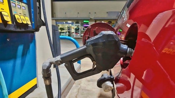 A car filling up with gasoline at a gas station, showing a close-up of the pump in the gas tank from a side view.