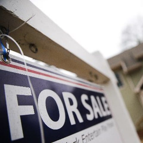 A "For Sale" sign hangs in front of an existing ho