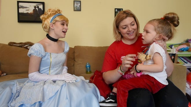 From the left, Madison Kelkis, sings a song from Cinderella to Ruby Hoffman, who has just turned 3, held by her mother Mindy. Ruby will be visited by seven Disney princesses, one each day, in a joint effort by Enchanted Teapot and Magical Moments.