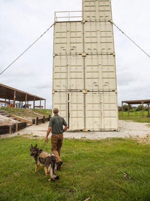 Brian Jones, chief executive officer, and his dog Sarge walk toward their sniper and rapelling building out by the shooting range.
