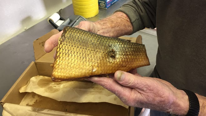 Dick Lixie holds a piece of smoked whitefish. The scar is from the nail the fish hung from as it was smoked.