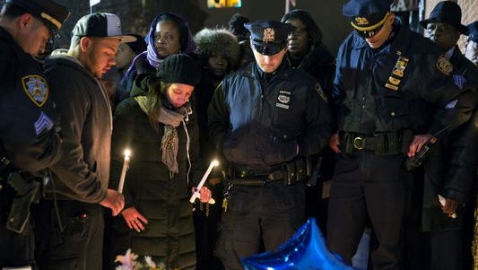 Police officers and other mourners stand in silence Sunday near the spot where two New York Police Department officers were shot and killed by an assailant.