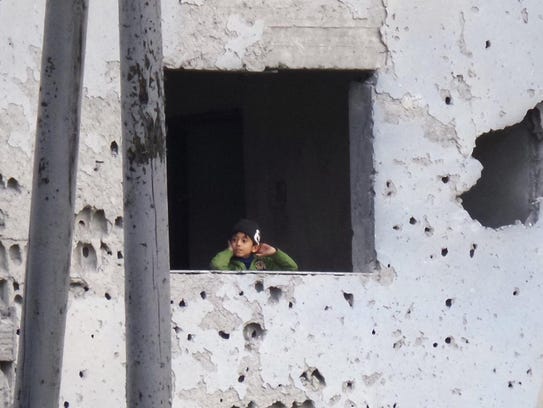 A Syrian boy looks out from a window inside the bullet-riddled