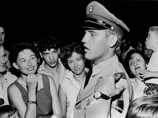While on his first furlough, Elvis Presley explains the insignia on his uniform to fans at the gates of Graceland on June 1, 1958. Elvis arrived late the previous night for a two-week leave. He was inducted into the U.S. Army on March 24, 1958.