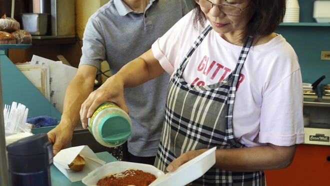 In this Thursday, March 14, 2019 photo, Belinda Lau, manager of the Wiki Wiki Drive Inn takeout restaurant in Honolulu, sprinkles cheese on an order of spaghetti in a styrofoam container.
