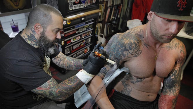 LoveHate Tattoo owner Joseph "Jet" DiProjetto, left, works on customer Anthony Caruso, right, in his shop on Alexander Street in the city.