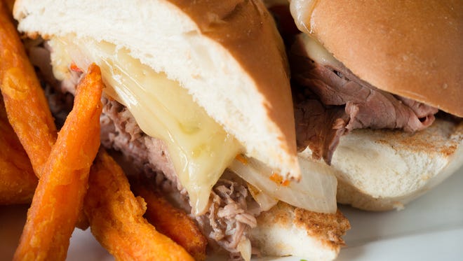 The French dip sandwich is piled with tender shaved roast beef, roasted red peppers, caramelized onions and melted Swiss cheese, and served with a salty jus and sweet potato fries.