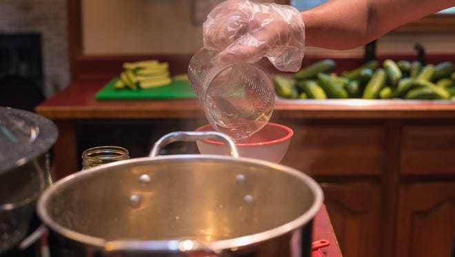 Mykel Brawley, owner of the Fort Collins Pickle Company, pours brine into a jar of sliced cucumbers and spice mix in her home kitchen on Thursday, August 10, 2017.