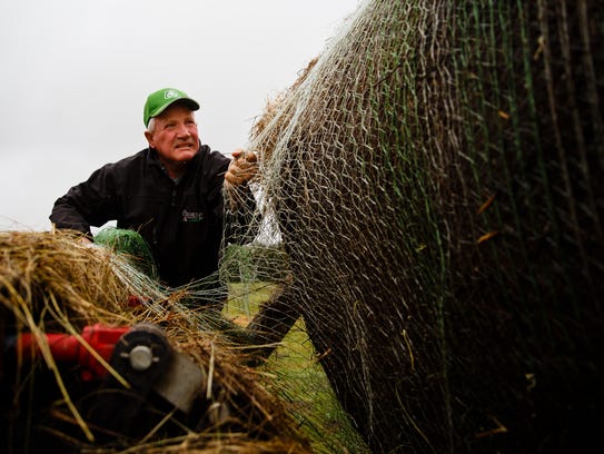 Farmer and Ranchers Ron Crumly cuts netting on a hay