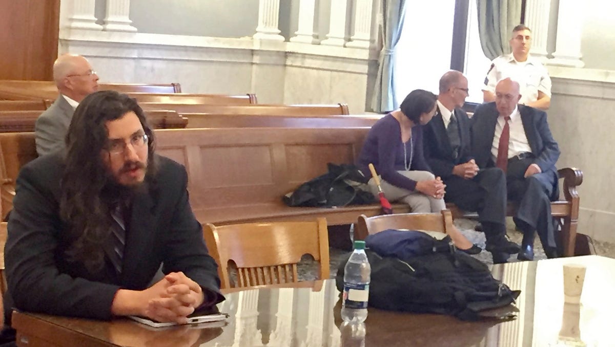 Michael Rotondo, left, sits during an eviction proceeding in Syracuse, N.Y., brought by his parents, Mark and Christina, of Camillus. The two parents confer with their lawyer, Anthony Adorante, in the court gallery behind. Rotondo told the judge Tuesday he knows his parents want him out of their Camillus home, near Syracuse. But he argued he's entitled to six months more time.