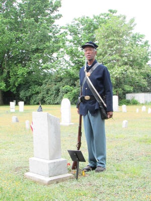 Richmond/Williston Rotary Club member Reg Melrose stands in uniform next to the grave of Civil War veteran Newell Cyrus Langeley at Morse Cemetery in Williston.