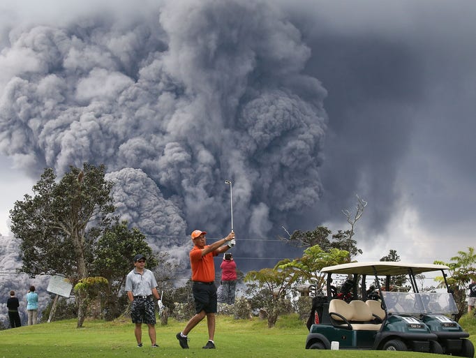 People play golf as an ash plume rises in the distance