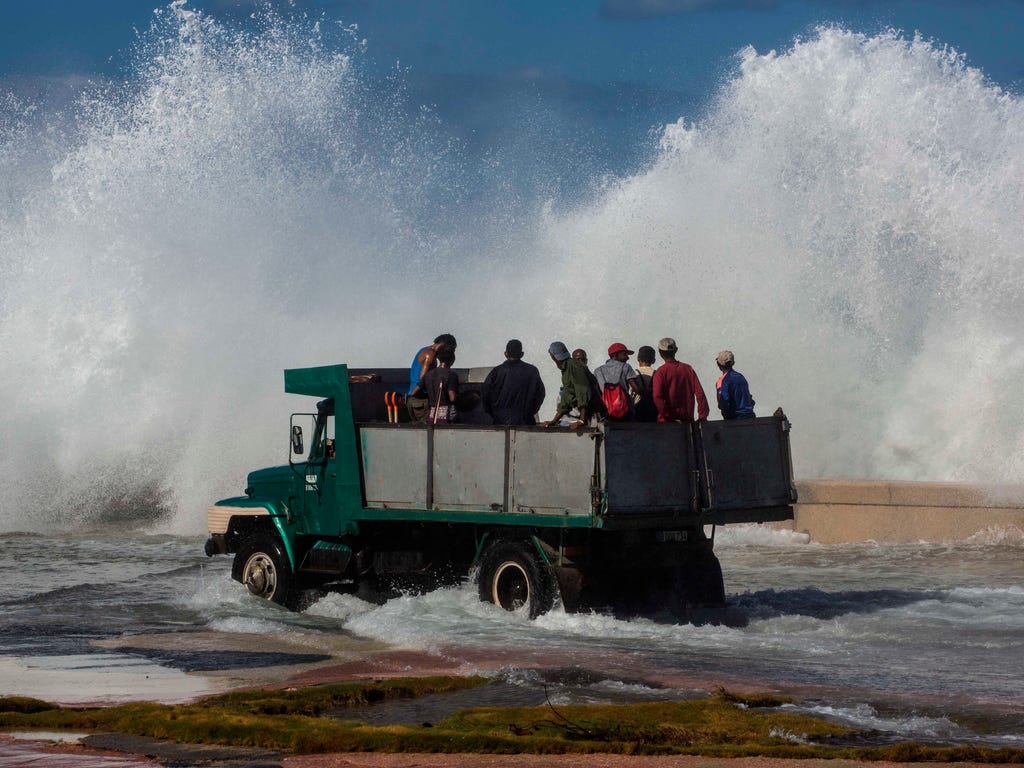 A dump truck carrying cleaning workers drives on Havana's malecon as a wave crashes on the seawall, in Cuba. Due to high winds and tides, the sea pushed over the seawall, flooding low parts of the Vedado neighborhood of Havana.