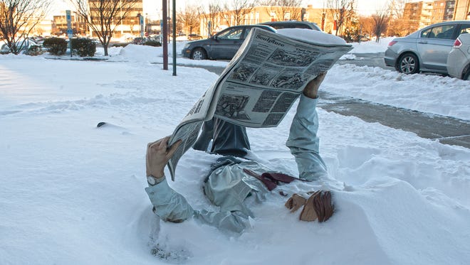 A bronze statue of a man reading a newspaper is covered with snow at the Cherry Hill Public Library.