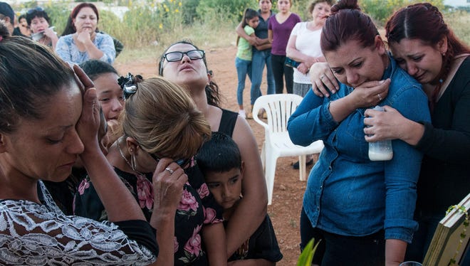 Selene Ramirez of Phoenix looks up while she hugs her family members praying at the shrine for her brother, Carlos Martinez, in Cananea, Sonora. Ramirez searched the desert of southern Arizona looking for her brother's remains.