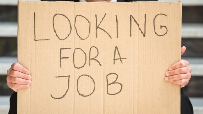 A businessman holding up a cardboard sign that reads, Looking for a job.