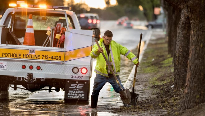 Visalia City worker Eddie Espirito clears a storm drain on Walnut Avenue at Cain Street on Wednesday, March 22, 2017. Police blocked the lane until the flood water subsided.