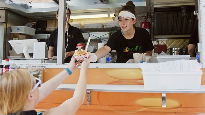 Katie Juroe, of Victor, hands out a plate of macaroni and cheese from the Macarollin food truck during the Ithaca Festival in August. The City of Ithaca allows temporary food truck permits for special events and is considering changing a vending policy to make the trucks a more permanent fixture on city streets.