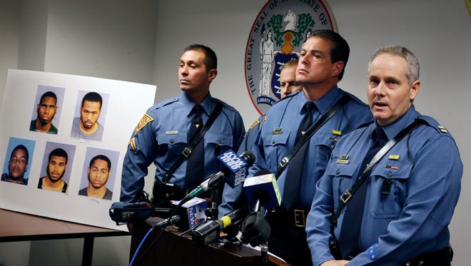 New Jersey State Police Cpt. Chris Leone, right, answers a question as he stands near a poster that shows Izyiah Plummer, top left,19, of Atlantic City, N.J., Aaron Evans, top right, 24. of Pleasantville,N.J.,Nathaniel Greenlee, bottom left, 21, of Bear, Del., Donovan Jackson, bottom center, 20, of Wilmington, Del., and Dwayne Morgan II, bottom right, 20, of Pleasantville,N.J.,  who along with three others were announced to have been arrested by police, Thursday, Aug. 14, 2014, in Atlantic City, N.J. State Police said eight people were arrested in the July 21 gunpoint robbery of Caesars Atlantic City that netted more than $180,000 and touched off a three-state manhunt.The search ended with a Delaware state trooper being shot; the bulletproof vest he was wearing saved his life. Others named by the police were Monique Kelly, 19, of Pleasantville,N.J.,  Lance Rogers, 20, of Atlantic City, N.J., and Myles Coleman, 23, of Atlantic City, N.J. (AP Photo/Mel Evans)
