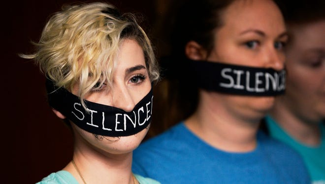 Survivors of sexual assaults by former MSU doctor Larry Nassar, Amanda Thomashow, left, 28, and Alex Neil-Sevier, 29, wear silence gags while listening to the Michigan State University Board of Trustees meeting, April 13, 2018, in East Lansing.